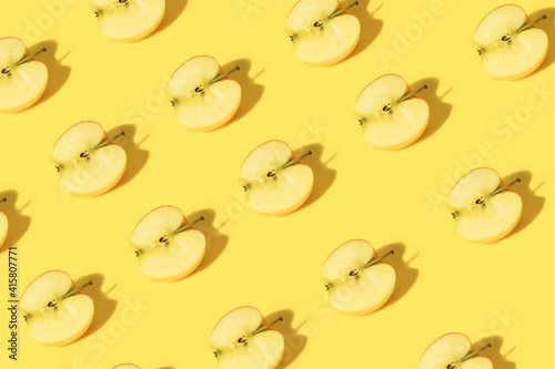 Creative pattern of apple halves on a pastel yellow background with trendy sunlight.