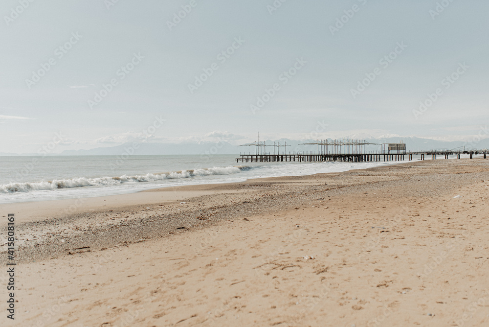 Meer, Wellen, leichte Wolken und Berge am Horizont, Sandstrand