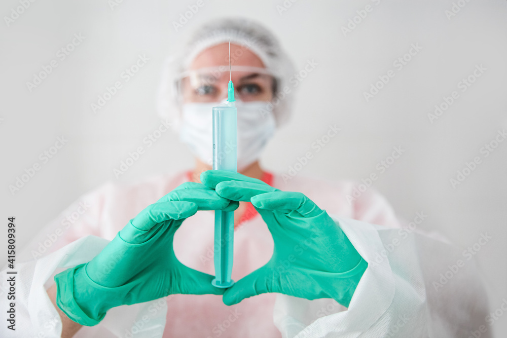 Naklejka premium A medical worker in a white robe, white cap and green gloves holds a syringe with a vaccine. Coronavirus concept