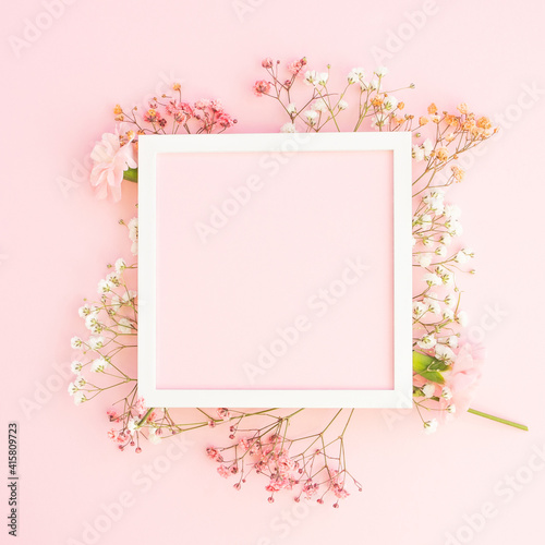 Creative spring greeting card design. Branches of white, and pink  gypsophila and fresh carnations  flowers with  square photo frame on pastel pink background. Birthday,  Mother's Day. Copy space.