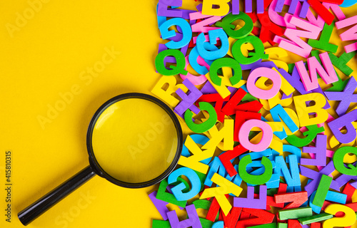 Magnifying glass with colorful alphabet on yellow background, Copy space.Education concept. photo