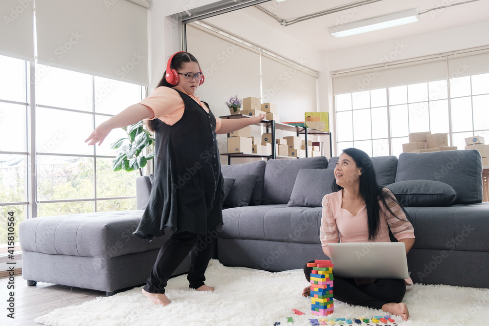 Asian mother using laptop and young girl with autism wearing headphone