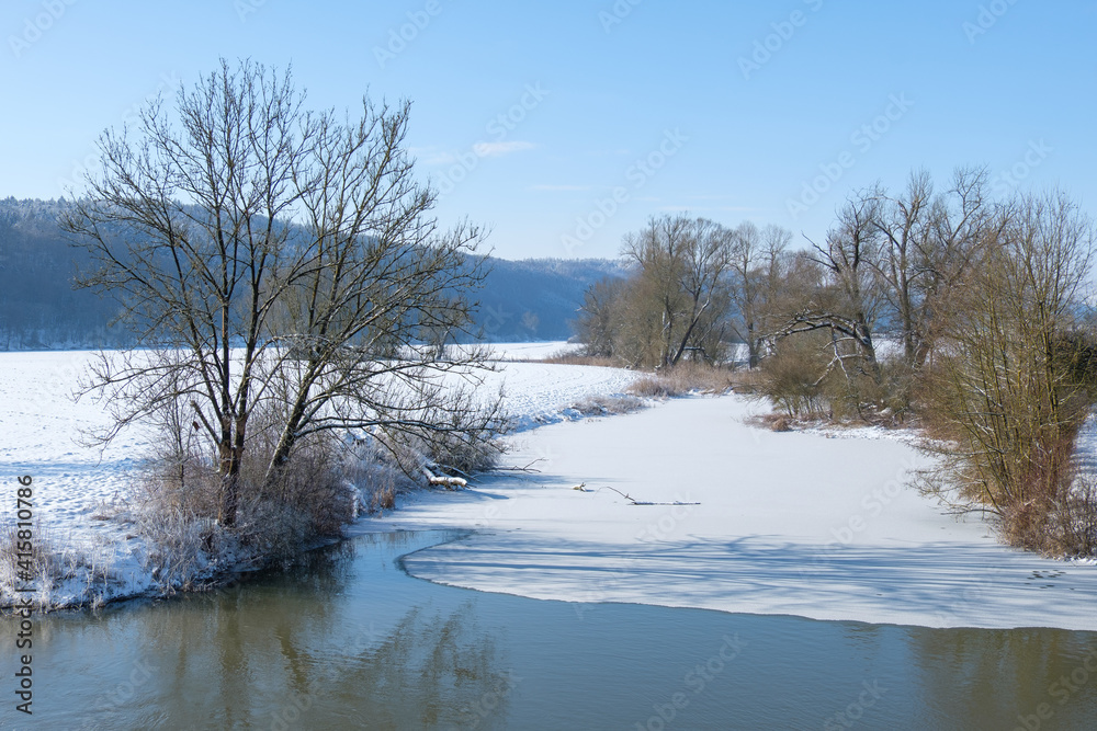 Winterliche Landschaft mit einem zugefrorenen Gewässer bei blauem Himmel und Schnee - rechts und links Ufer Winterliche Landschaft mit einem zugefrorenen Gewässer bei blauem Himmel und Schnee - rechts und links Ufer