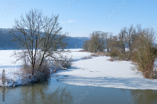 Winterliche Landschaft mit einem zugefrorenen Gewässer bei blauem Himmel und Schnee - rechts und links Ufer