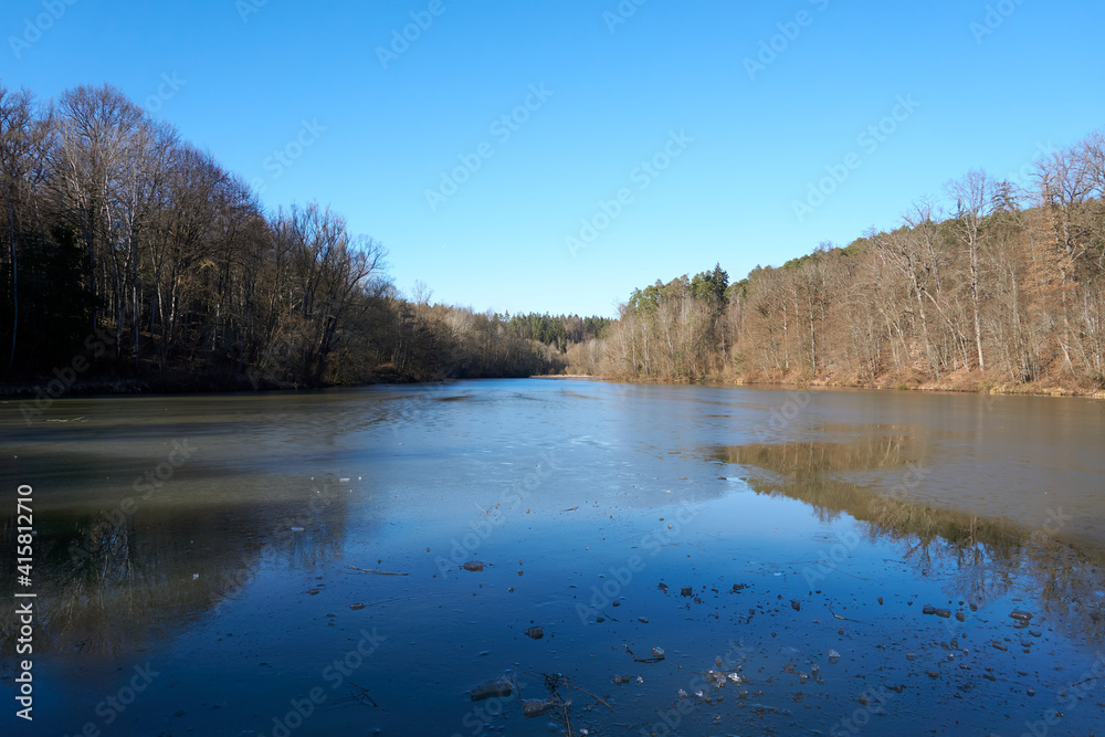 artificial lake with a frozen surface surrounded by trees in the forest artificial lake with a frozen surface surrounded by trees in the forest