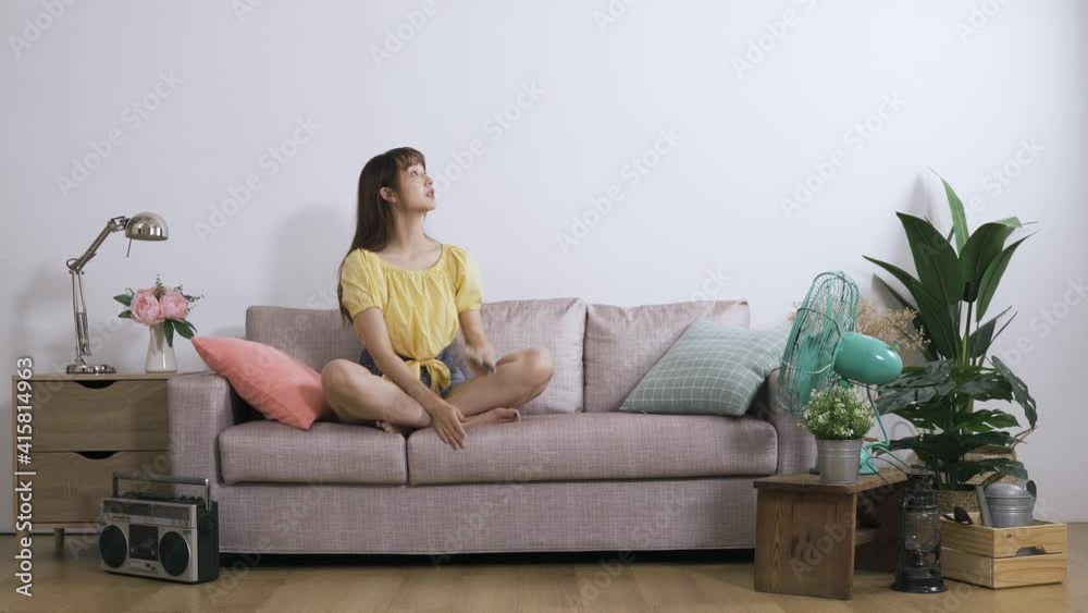 asian lady fanning herself with hands is tuning on the air conditioning with a remote control to beat summer heat on the couch over white background.