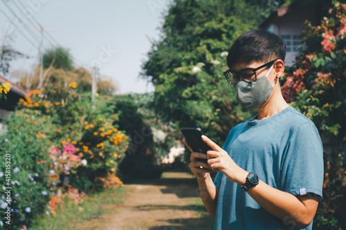 Asian woman wear fabric facial masks and used mobile or smartphones to check news of coronavirus in the garden. Social distance and work from home.