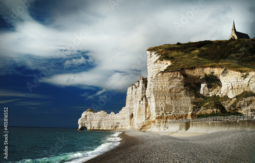 A rocky chalk cliffs near the emerald ocean. Spectacular view of the Etretra cliffs with natural arches and Chapelle Notre-Dame de la Garde on the top.     