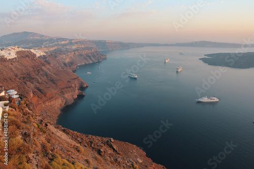 Bay in the rays of the setting sun with cruise liners. Santorini coastal landscape.