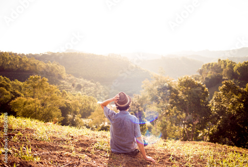 Young man sitting on the top of a mountain watching the sunset while adjusting his hat.