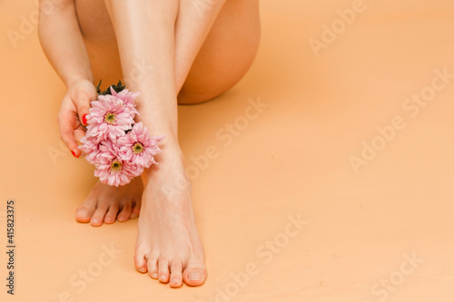 Close up photo of enjoying her beauty. Attractive young woman in underwear posing while sitting with flower against beige background.