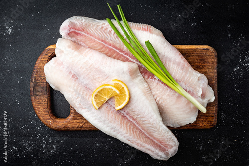 Foto Fillet of raw pangasius fish with lemon and green onion on cutting board on dark background