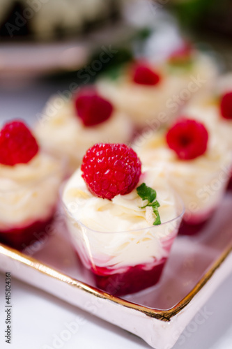 Single serving mousse desserts on a candy bar of a wedding banquet. Catering, festive buffet. Tasty mousse dessert with jelly and berries in a glass on light background close up. Delicious dessert
