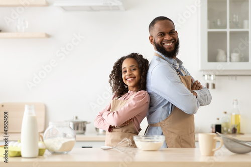 Happy black man and his child daughter posing in kitchen