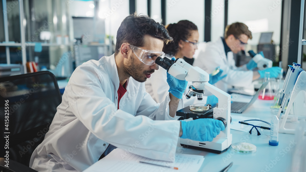 Fototapeta premium Medical Science Laboratory: Row of Diverse Team of Multi-Ethnic Young Scientists Looking Under Microscope, Analyze Chemicals, Talk, Solving Problems. Biotechnology Specialists working in Advanced Lab
