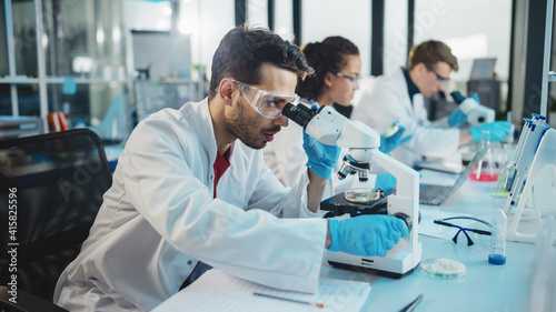 Medical Science Laboratory: Row of Diverse Team of Multi-Ethnic Young Scientists Looking Under Microscope, Analyze Chemicals, Talk, Solving Problems. Biotechnology Specialists working in Advanced Lab