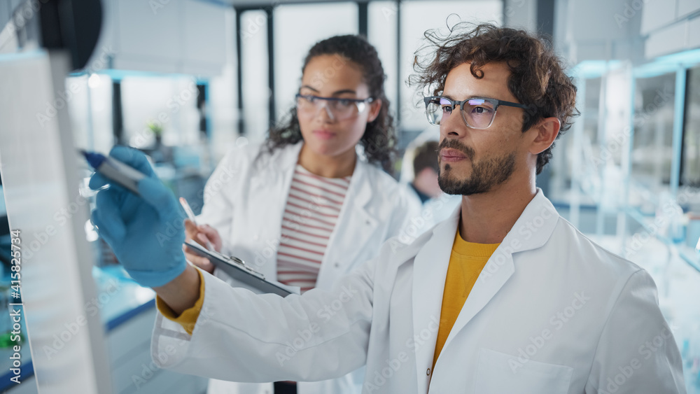 Fototapeta premium Medical Science Laboratory: Handsome Latin Male Scientist Writes Detailed Project Data Analysis on the Board, His Black Female Colleague Talks. Young Scientists Solving Problems.