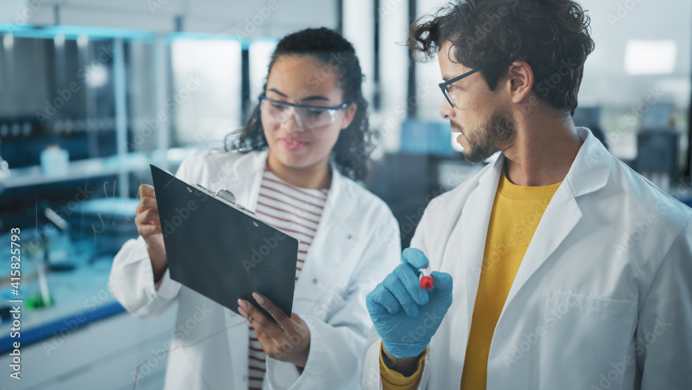 Medical Science Laboratory: Handsome Latin Male Scientist Doing Project Data Analysis, His Black Female Colleague Checks Information on Clipboard. Young Scientists Solving Problems