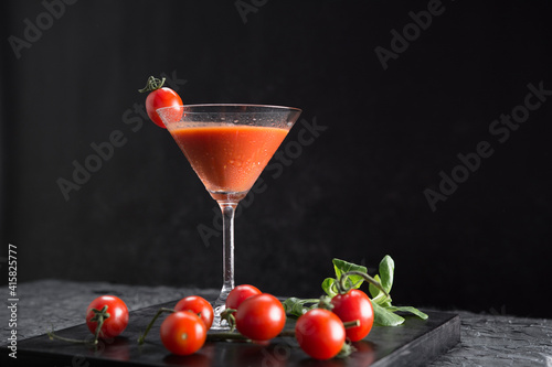 Sopa de tomate fría española, gazpacho, hecha con tomate, pepino, pimiento, cebolla, ajo y aceite de oliva servida en copa de cóctel con tomates cherry sobre fondo negro