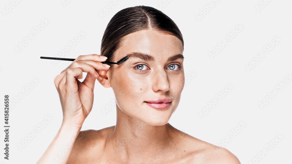 young woman with clean face looking at camera and styling eyebrow isolated on white