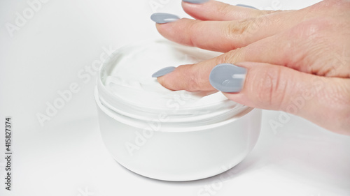 cropped view of woman applying cosmetic cream from container on white