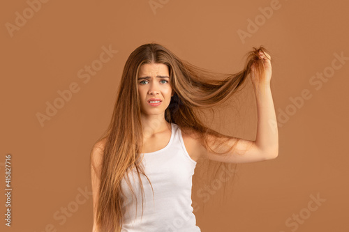 Photography Frustrated millennial woman showing her damaged long hair on brown studio background