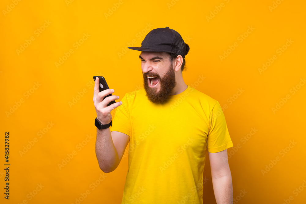 Photo of angry bearded man screaming at smartphone while talking with someone.