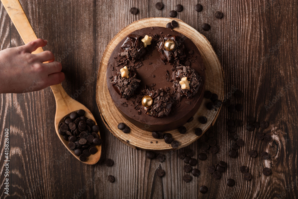 Overhead view of the chocolate cake, with chocolate chips, a hand on the spoon