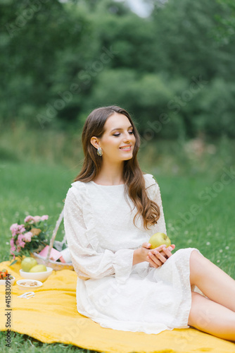 Smiling caucasian teen girl sitting outdoors. Creative artistic young woman wearing casual clothes having a picnic with apple on summer day.
