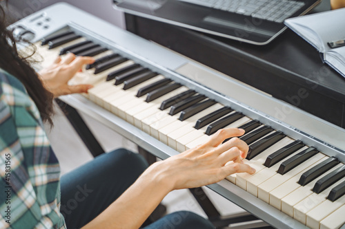Close up of unrecognizable young woman playing electric piano teaching remotely using laptop while working from home. Online education and leisure concept.
