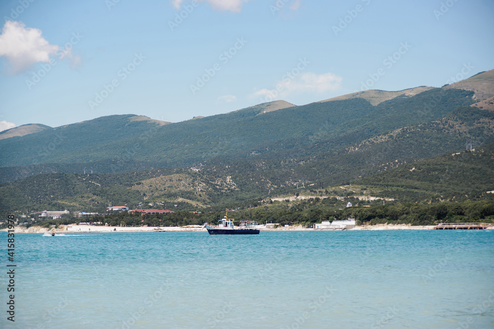 side view of fishing trawler boat without people in black sea bay on beach, mountains, and sky background, horizontal outdoors stock photo image