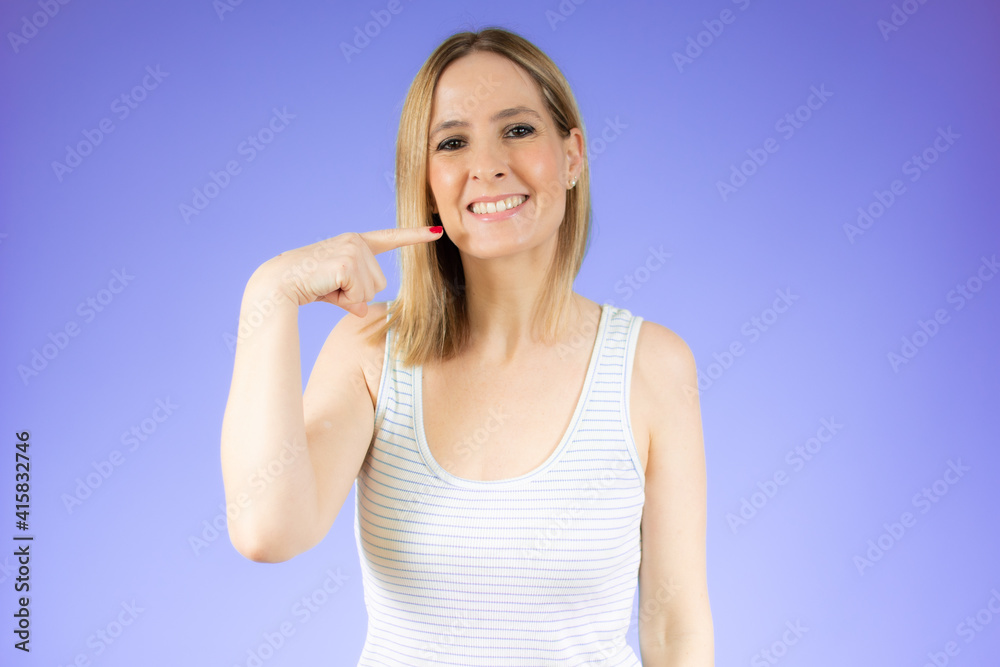 Young beautiful woman standing over purple isolated background smiling cheerful showing and pointing with fingers teeth and mouth. Dental health concept.