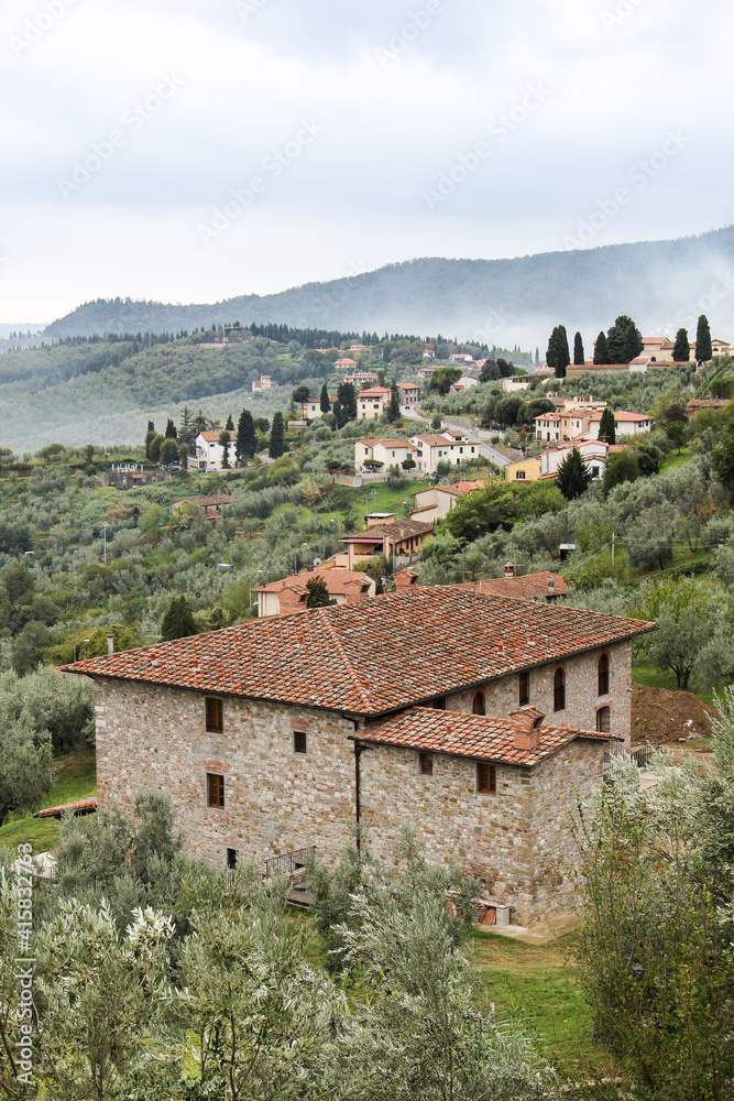 Tuscan hills with villas, olive fields and farms. Old villa in the foreground in the village of Carmignano near Florence, Italy. In the background there are hills in fog, a cloudy sky, tranquility.