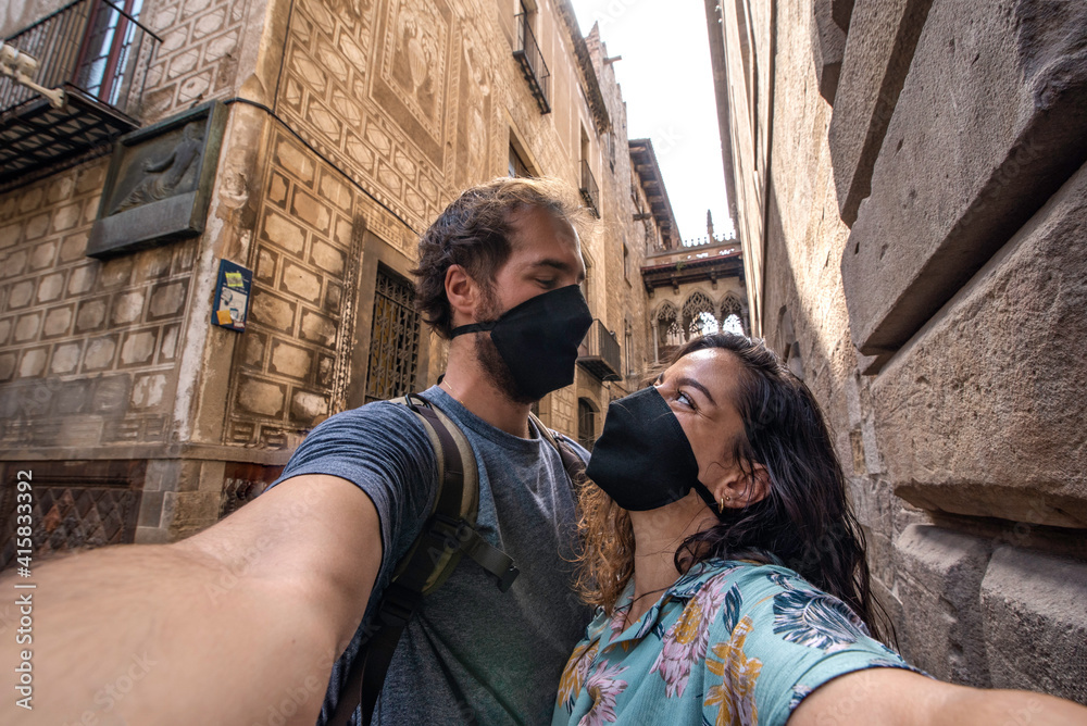 Couple of travelers take a selfie with an anti Covid 19 mask while visiting the Gothic quarter of the city of Barcelona, Spain 