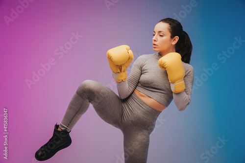 Photo of strong sportswoman in boxing gloves prepared higt kick. isolated on gradient studio background in neon light. Beautiful caucasian woman practicing photo