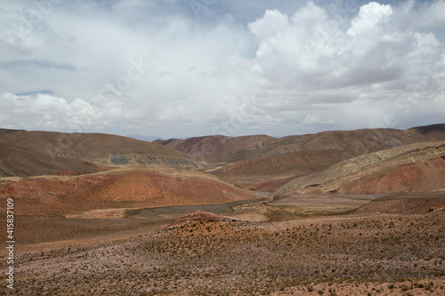 Andes mountain range deserted scenery under a beautiful cloudy sky. The arid land, meadow and colorful hill. 