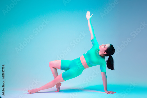 Plank. Young sportive woman training isolated on gradient studio background in neon light. athletic and graceful. Modern sport, action, motion, youth concept. Beautiful caucasian woman practicing.