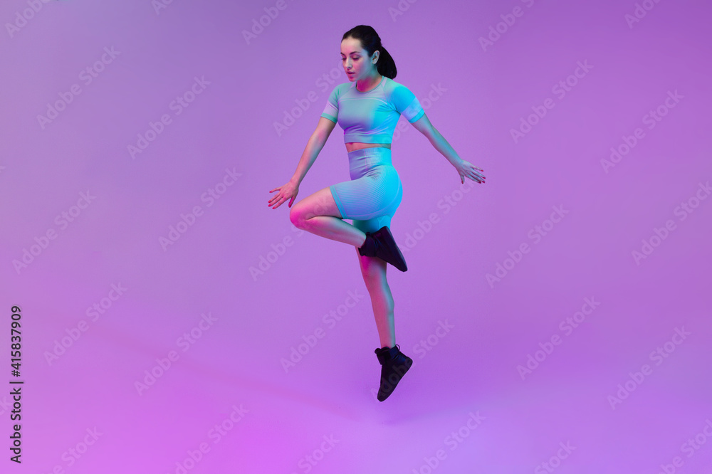 Young sportive woman training isolated on gradient studio background in neon light. athletic and graceful. Modern sport, action, motion, youth concept. Beautiful caucasian woman practicing