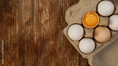 White eggs carton and cracked egg half with yolk top view on wooden background. Easter and healthy food breakfast cooking concept