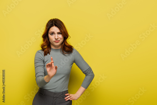 displeased woman standing with hand on hip and pointing with finger while showing no sign on yellow photo