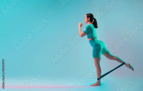 Young fit and sportive woman with resistance band for legs on gradient background. Fit sportswoman posing. Perfect body ready for summertime. Beauty  resort  sport concept