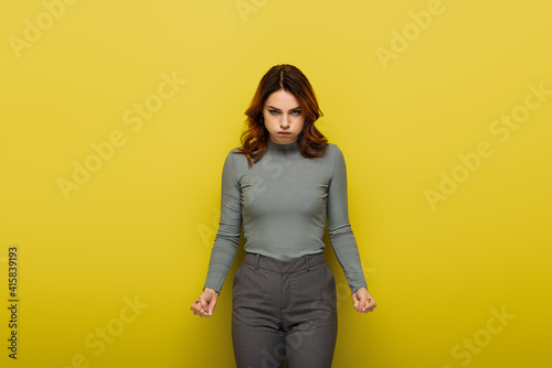 displeased woman puffing cheeks while looking at camera on yellow