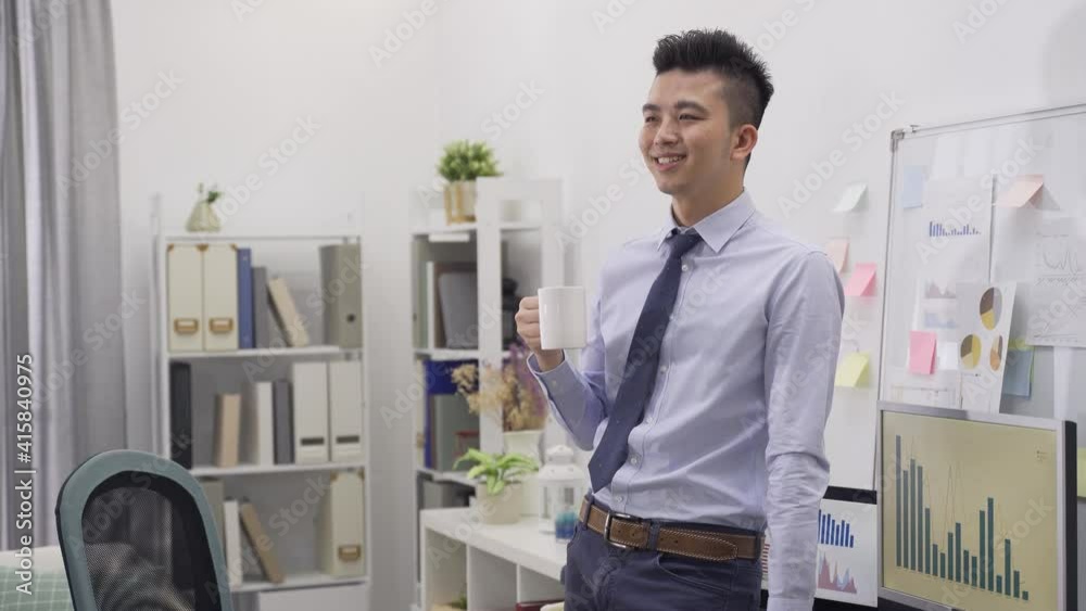 happy male employee standing leaning on desk while relaxing and looking into distance with hot drink in his bright office. happy male employee standing leaning on desk while relaxing and looking into distance with hot drink in his bright office.