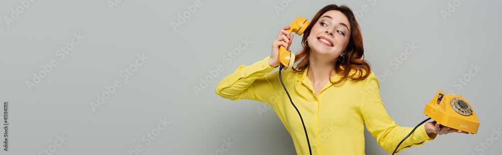 cheerful woman talking on retro phone while looking away on grey, banner cheerful woman talking on retro phone while looking away on grey, banner