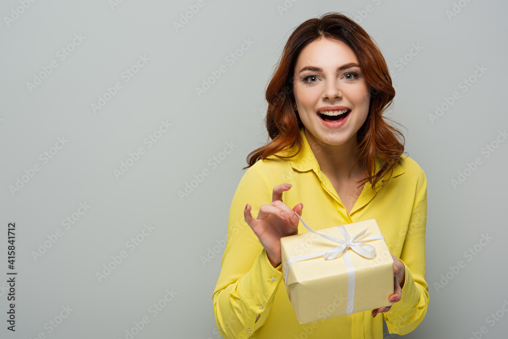 Obraz premium cheerful woman looking at camera while opening gift box on grey