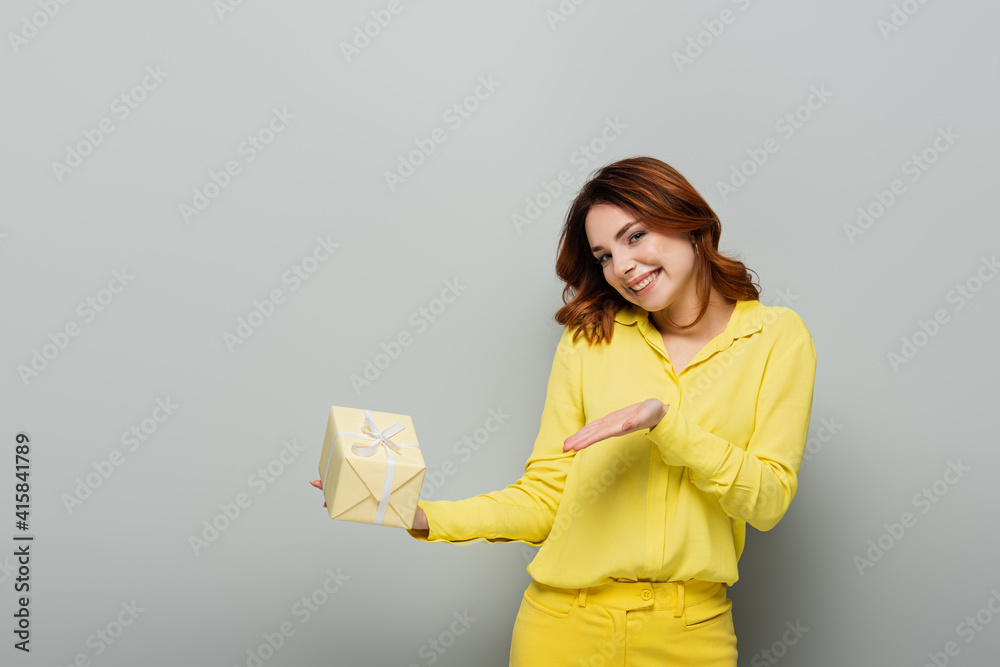 excited woman smiling at camera while pointing at gift box on grey excited woman smiling at camera while pointing at gift box on grey
