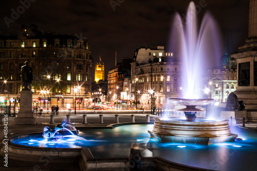 Illuminated fountain in Trafalgar Square taken at night time.