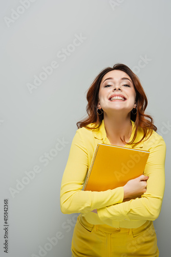 cheerful woman with notebook smiling at camera on grey