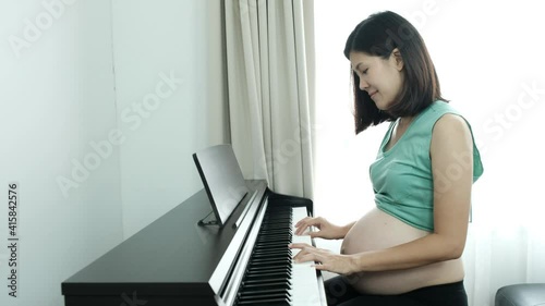 Asian pregnant woman playing music with the piano for her expecting baby