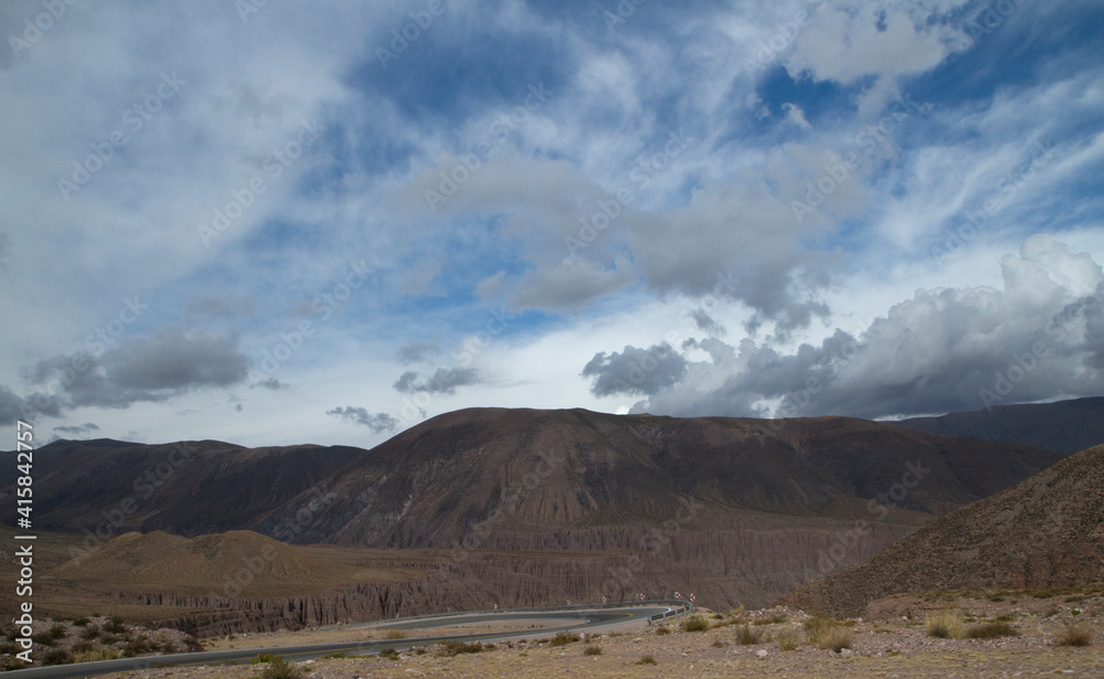 Traveling across the Andes mountain range under a magical sky. View of the desert road across the rocky hills and arid desert.	
